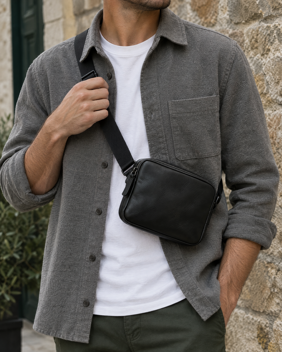 Homme ajustant la sangle d'une petite sacoche bandoulière en cuir noir Image